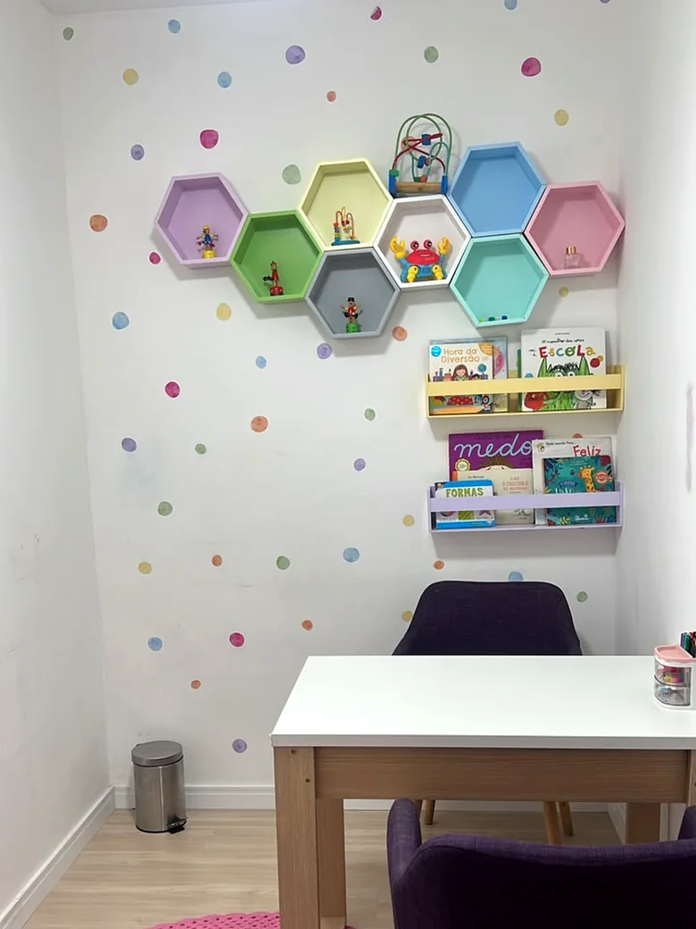 Sala lúdica da Life Kids com prateleiras hexagonais coloridas, parede de bolinhas, livros infantis e mesa de atendimento